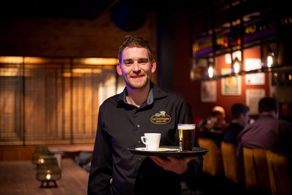 Medewerker van Posta7 brengt koffie en bier naar de tafel in de lounge