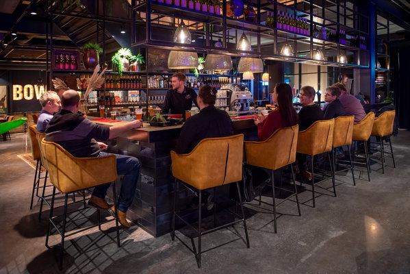 Gasten aan de bar in de lounge van Posta7 met cognac-kleurige barkrukken