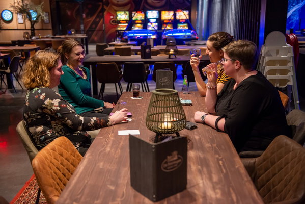 Vriendinnen aan tafel in de lounge van Posta7 met de arcadekasten op de achtergrond