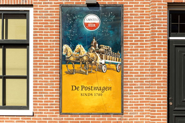 Nostalgisch Amstel-reclamebord met postkoets op de bakstenen gevel van De Postwagen