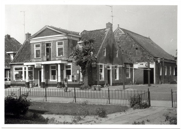 Zwart-witfoto van De Postwagen met hekwerk en de buurpanden aan de Hoofdstraat