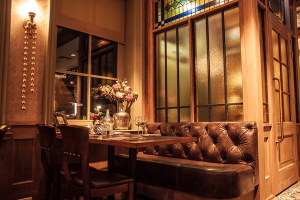 Sfeervolle tafel met bloemen en lederen bank bij het raam in restaurant De Postwagen