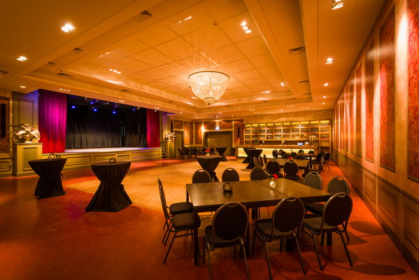 Zaal 't Koetshuis van De Postwagen met podium, rode gordijnen en statafels