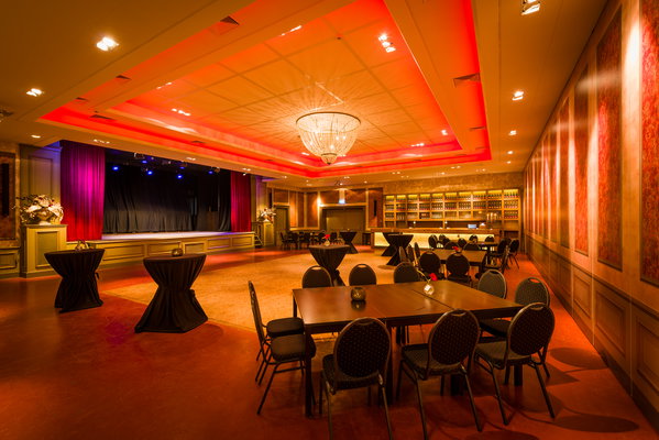 Zaal 't Koetshuis met rode sfeerverlichting en podium