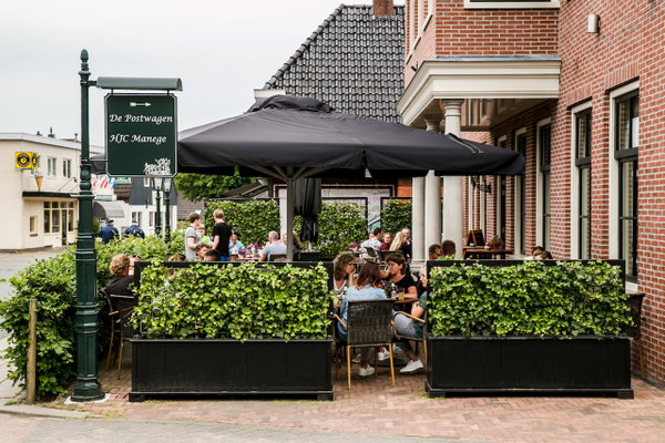 Terras van De Postwagen met parasols en gasten aan de Hoofdstraat in Tolbert