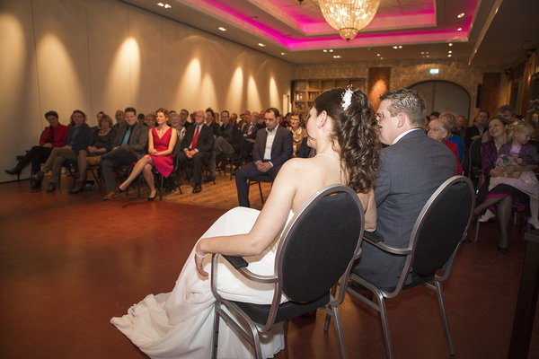 Bruidspaar op de eerste rij tijdens de ceremonie in de zaal van De Postwagen