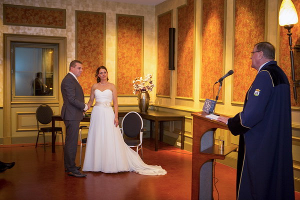Bruidspaar staat voor de trouwambtenaar tijdens de ceremonie bij De Postwagen