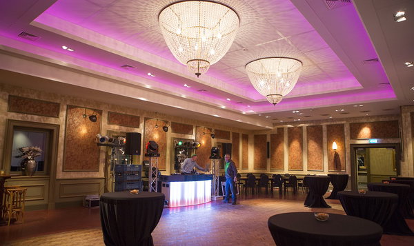 Feestzaal van De Postwagen met kroonluchters, dj-booth en roze sfeerverlichting klaar voor het bruiloftsfeest