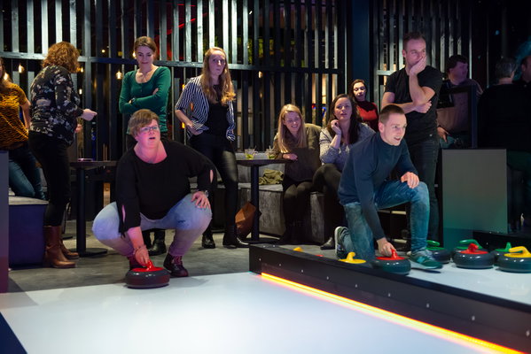 Deelnemers schuiven een curlingsteen over de baan tijdens Fun Curling bij Posta7