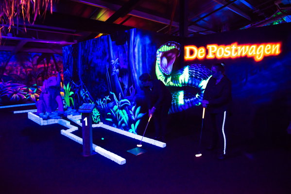 Spelers putten op de glow in the dark midgetgolfbaan van Posta7 bij de lichtgevende slang