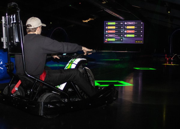 Rijder op een elektrische driftkart met het scorebord op de achtergrond bij Posta7